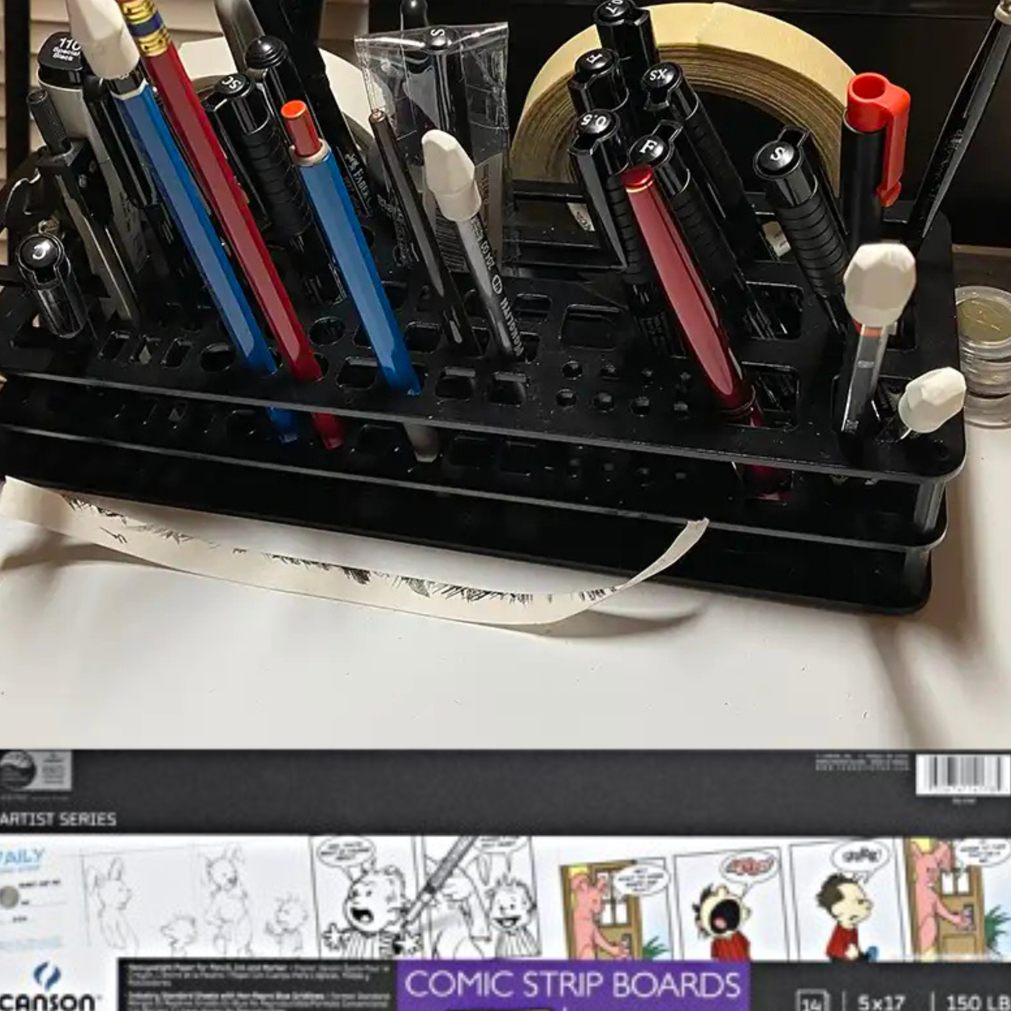 Close-up of Jim Cox's drawing tools, including technical pens, pencils, blending stumps, and comic strip boards on his desk